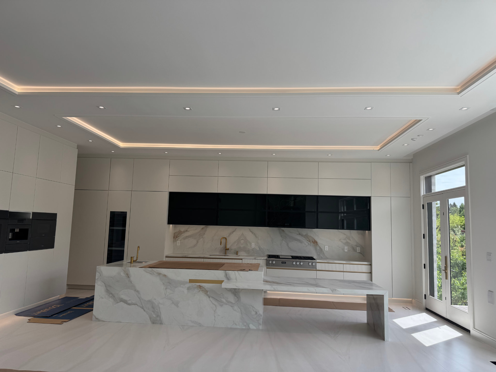 Modern kitchen interior with a marble island, black cabinetry and warm cove lighting